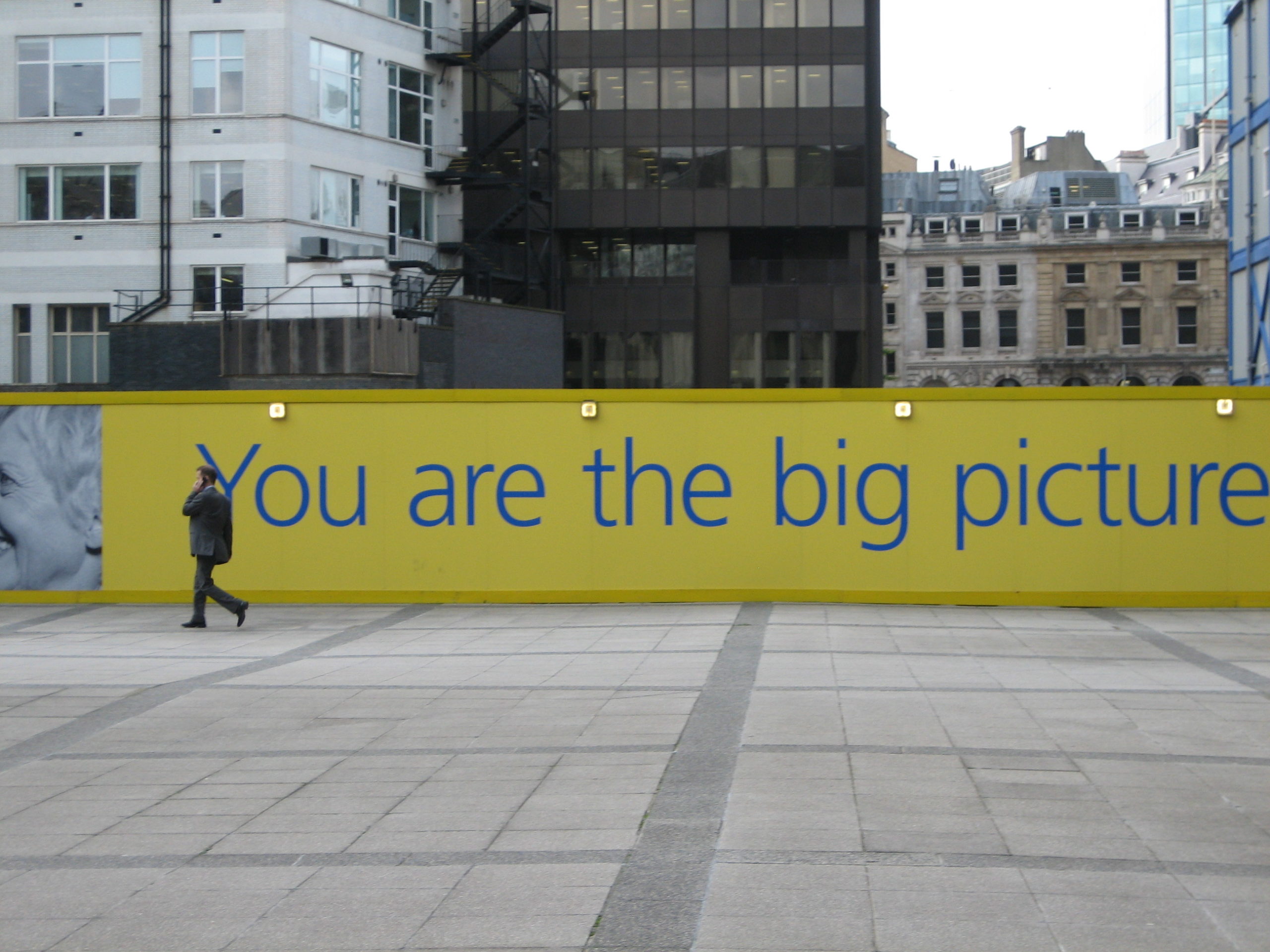 Pedestrian walking past a motivational urban billboard stating 'You are the big picture