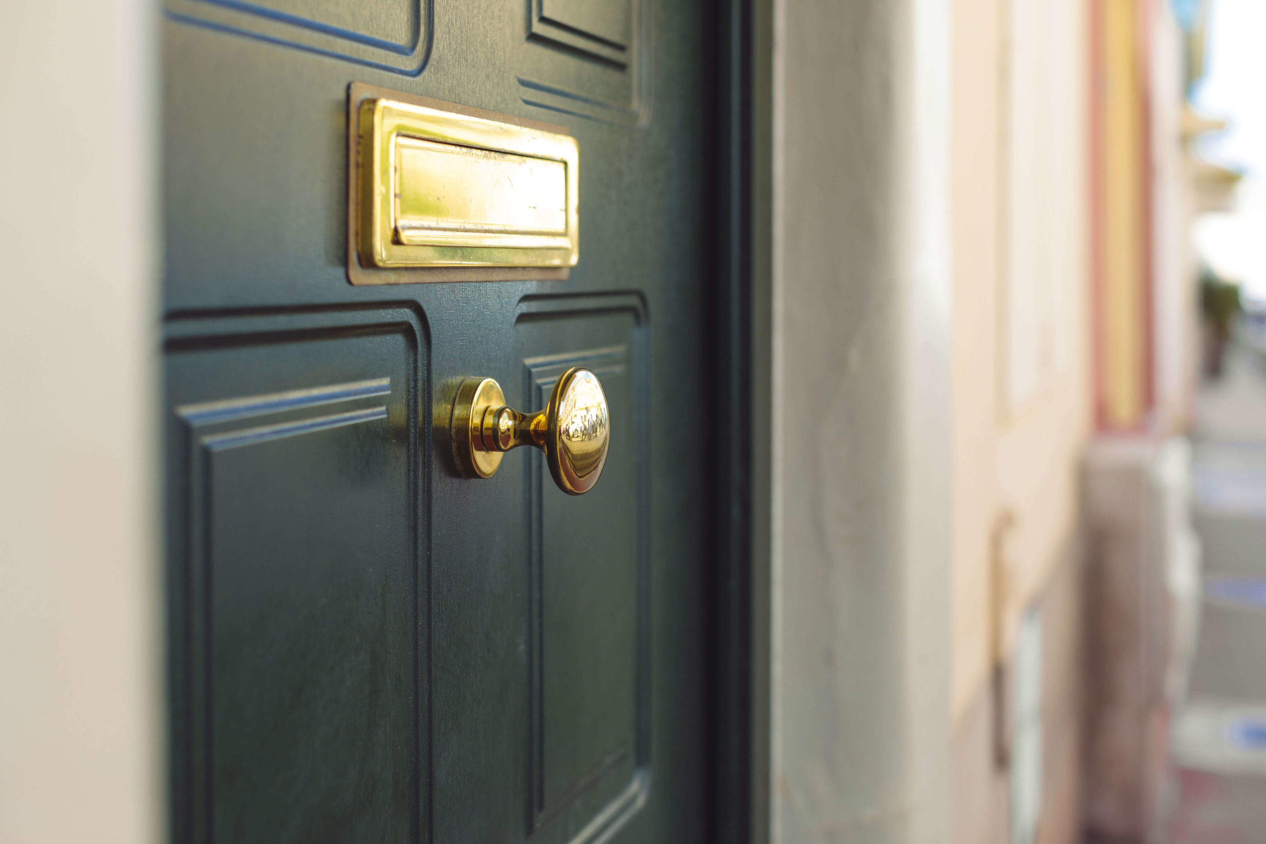 Close up of a green front door with a gold door knocker and letterbox