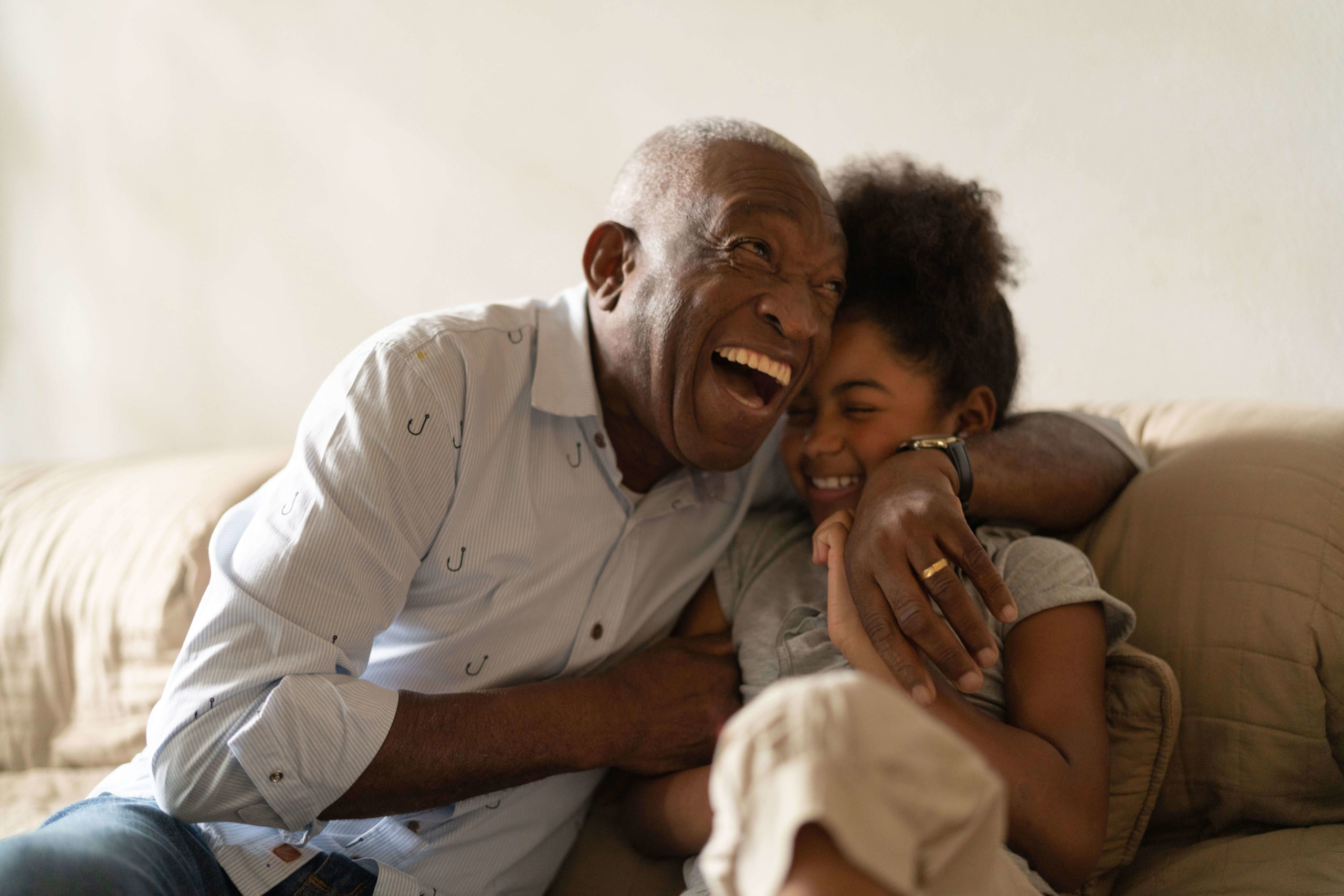 A grandparent laughing and hugging his grand daughter
